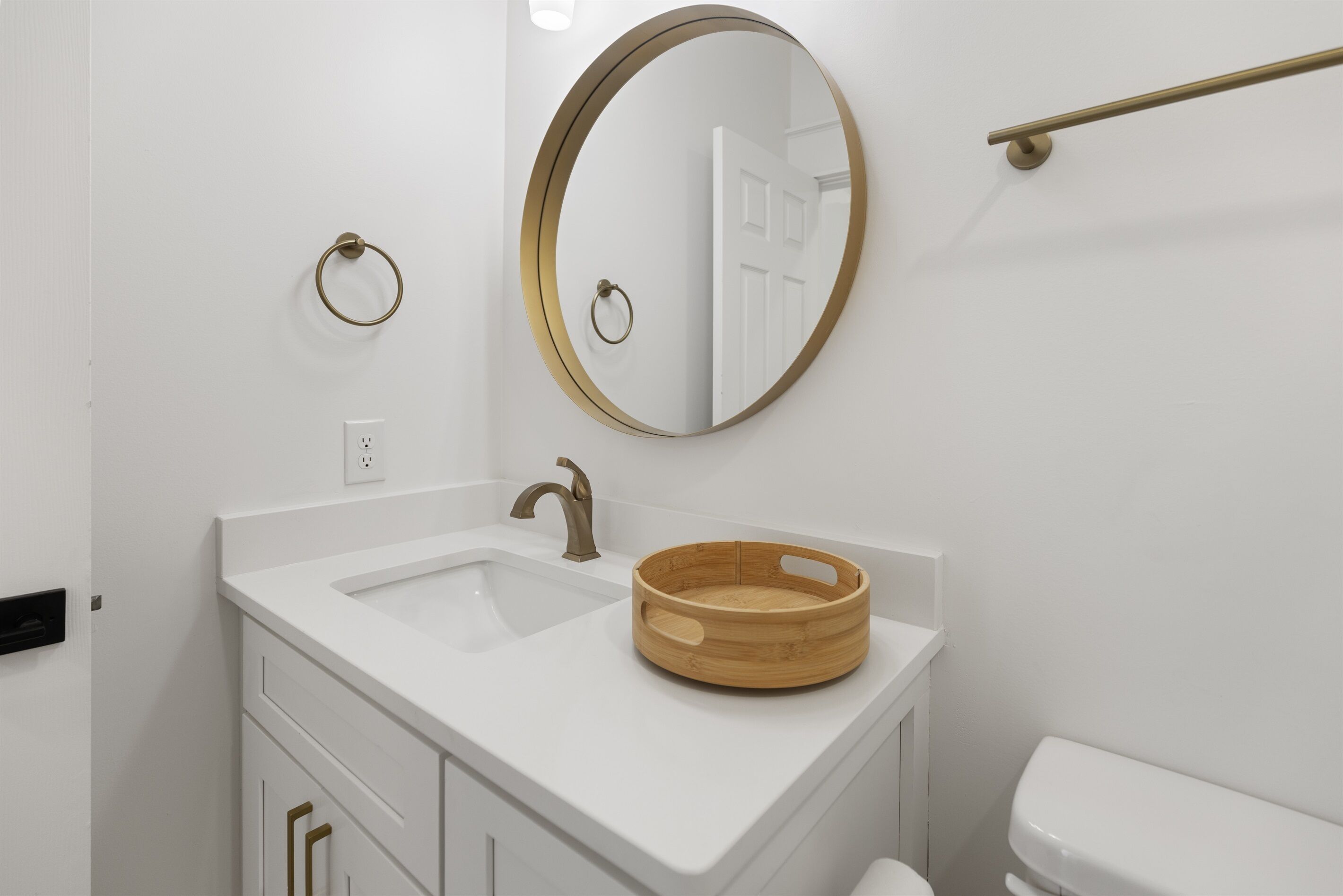 A bathroom with a white sink, a round mirror, and a wooden bowl on the countertop.