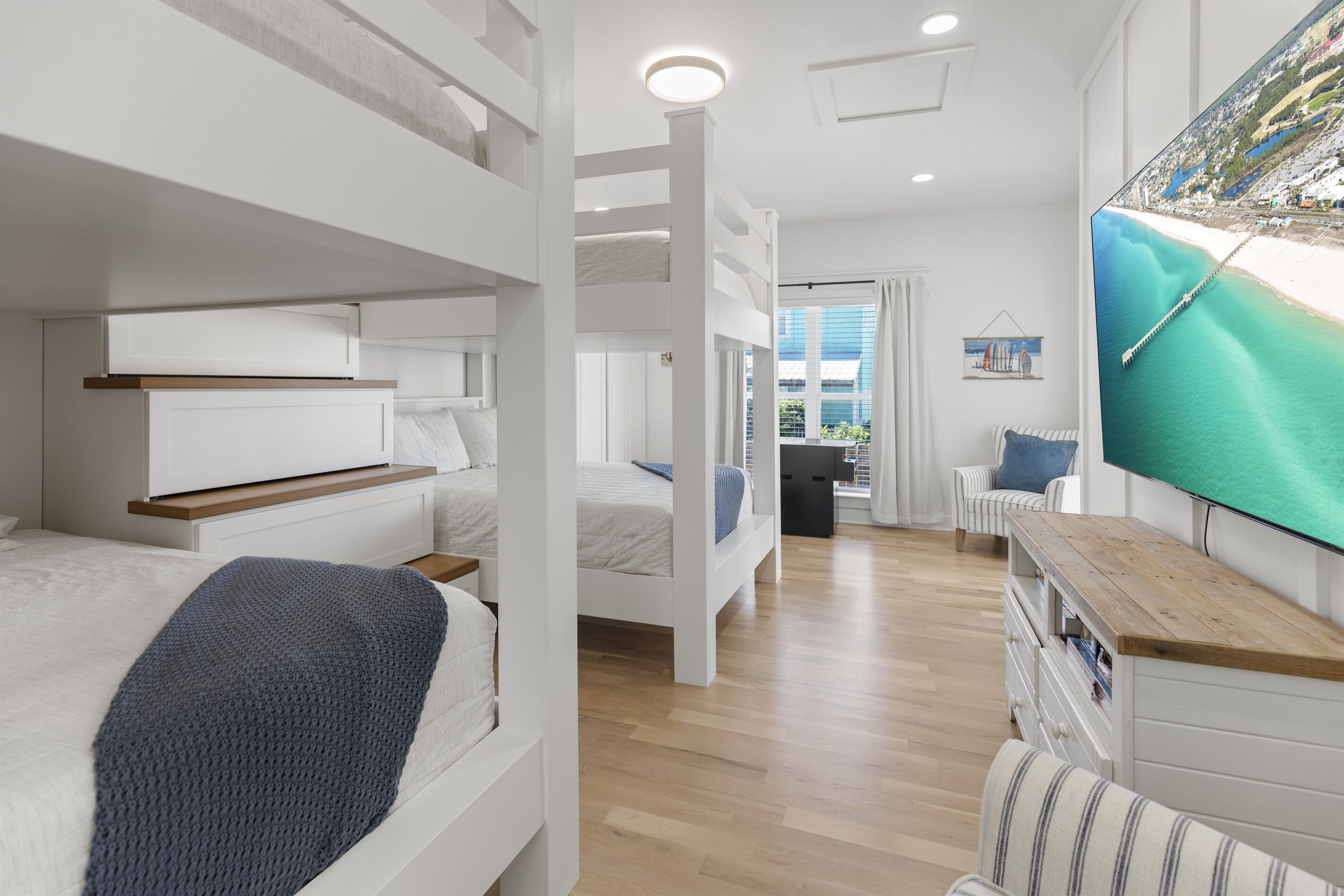A modern hotel room with bunk beds, a TV, a wooden floor, and a view of a beach.