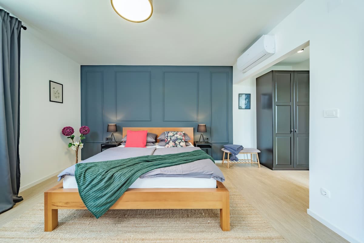 Ein modernes Schlafzimmer mit einem hölzernen Bett, einem Nachttisch, einer Lampe und einer Wand-Klimaanlage.