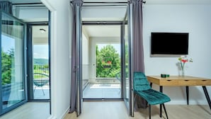 A modern room with a sliding glass door leading to a balcony, a wooden desk with a chair, and a flat-screen TV mounted on the wall. - PLITVICE LACUS (Rakovica)