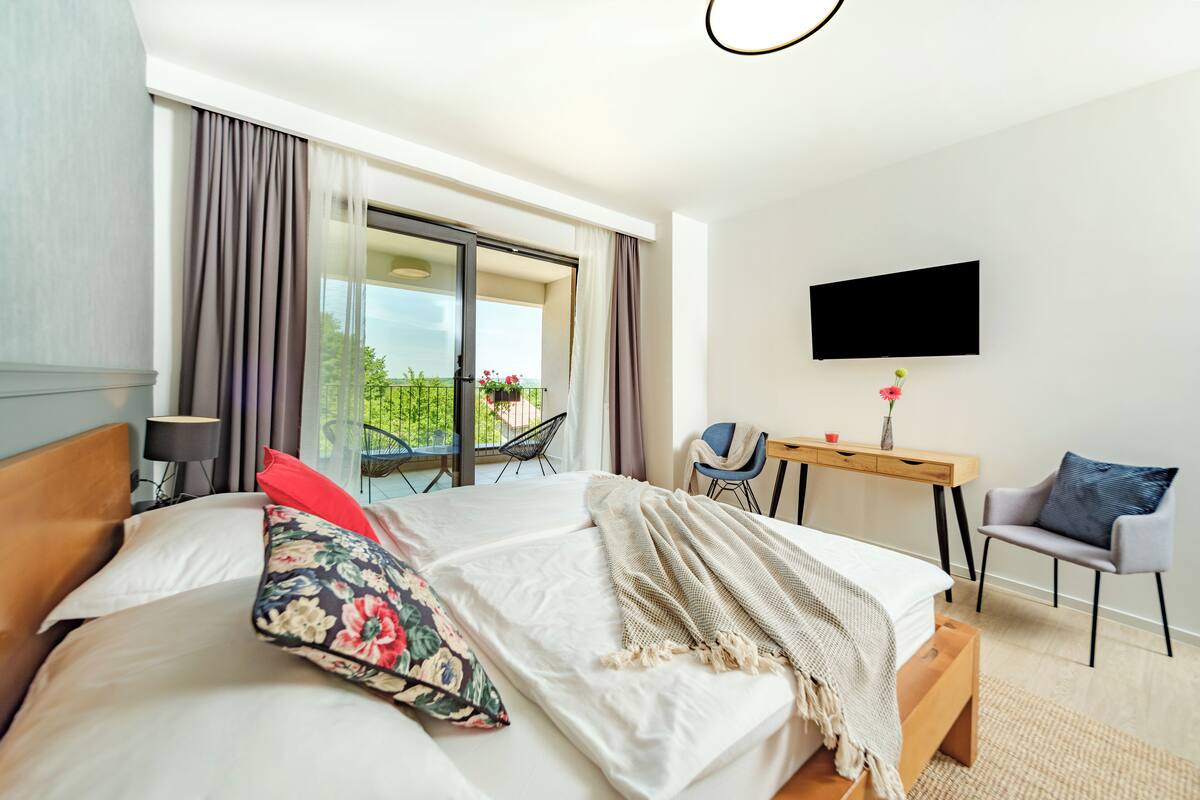 Ein Hotelzimmer mit Bett, Schreibtisch, Sessel, Fernseher und einem Balkon mit Blick.