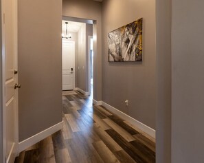 Un pasillo con piso de madera, una puerta blanca y un cuadro en la pared.