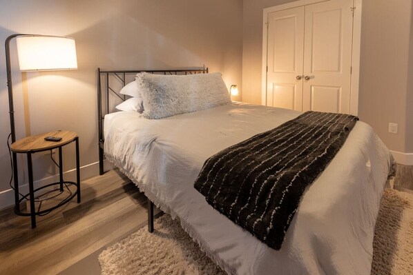 Une chambre à coucher avec un lit, une lampe de chevet, une petite table et une porte.