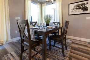 A dining area with a rectangular table, four chairs, a potted plant, and a framed picture on the wall.