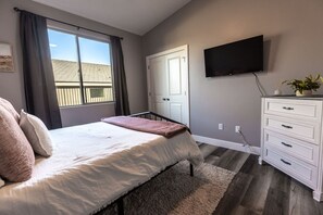 Un dormitorio con cama, cómoda, televisor y ventana con cortinas.