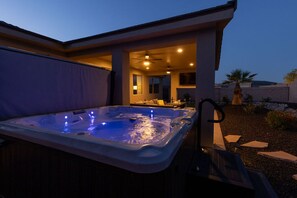 A hot tub in a covered outdoor area with a patio and a view of the house.