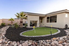 Una casa moderna con un jardín ajardinado que incluye un putting green y una palmera.