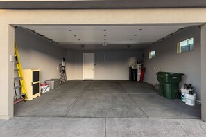 A garage with a concrete floor, a white door, and various items like a ladder, a toolbox, and a green trash bin. - Double Bogey Jackpot by J and Amy BL991951 (Mesquite)
