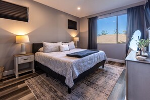 A modern bedroom with a large bed, bedside lamps, a desk, and a view of the outdoors.