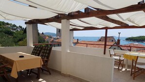 A terrace with a table and chairs, a view of the sea, and buildings in the background. - Apartment Luca (Vodice)
