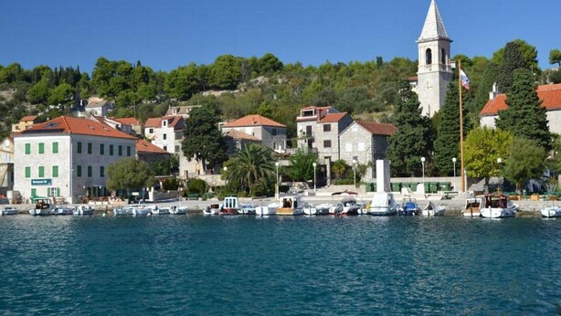 A coastal town with a prominent church tower, several buildings with red roofs, and a marina with boats. - Apartment Luca (Vodice)
