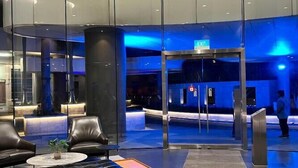 A modern lobby with a glass entrance, leather seating, and a blue-lit reception area.