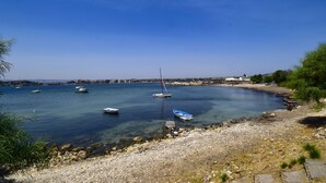 A coastal scene with boats on calm waters, a rocky shoreline, and a distant cityscape. - Zuccheri Canditi by Interhome (Augusta)