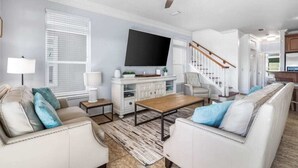 A living room with a sofa set, a coffee table, a TV, and a staircase. - Sea Lover - 5 BR Gulf View Getaway with Pool, Pets (Panama City BeachF)