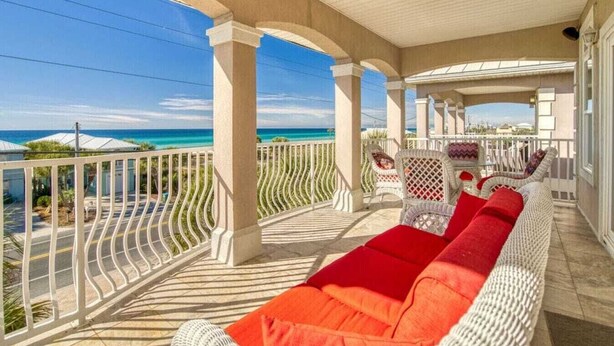 A covered balcony with white wicker furniture and red cushions, overlooking a clear blue sea. - Sea Lover - 5 BR Gulf View Getaway with Pool, Pets (Panama City BeachF)