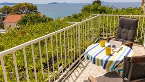 Un balcon avec vue sur la mer, une table recouverte d’une nappe à rayures et du mobilier d’extérieur.