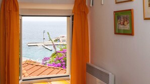 Une pièce avec un téléviseur fixé au mur, une fenêtre avec des rideaux, un radiateur et une chaise.