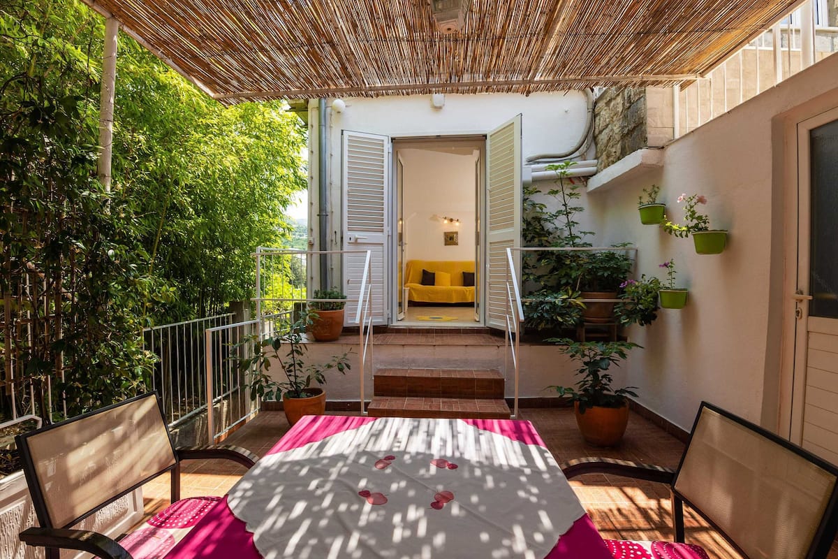 Eine Terrasse im Freien mit Tisch, Stühlen, einem Korbschirm und Topfpflanzen.