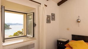 Une chambre avec une fenêtre donnant sur un plan d’eau, un lit recouvert d’une couverture à rayures, une table de chevet et un luminaire fixé au mur.