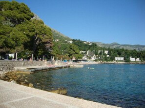 A coastal area with a stone pier extending into calm waters, surrounded by lush greenery and buildings in the background.