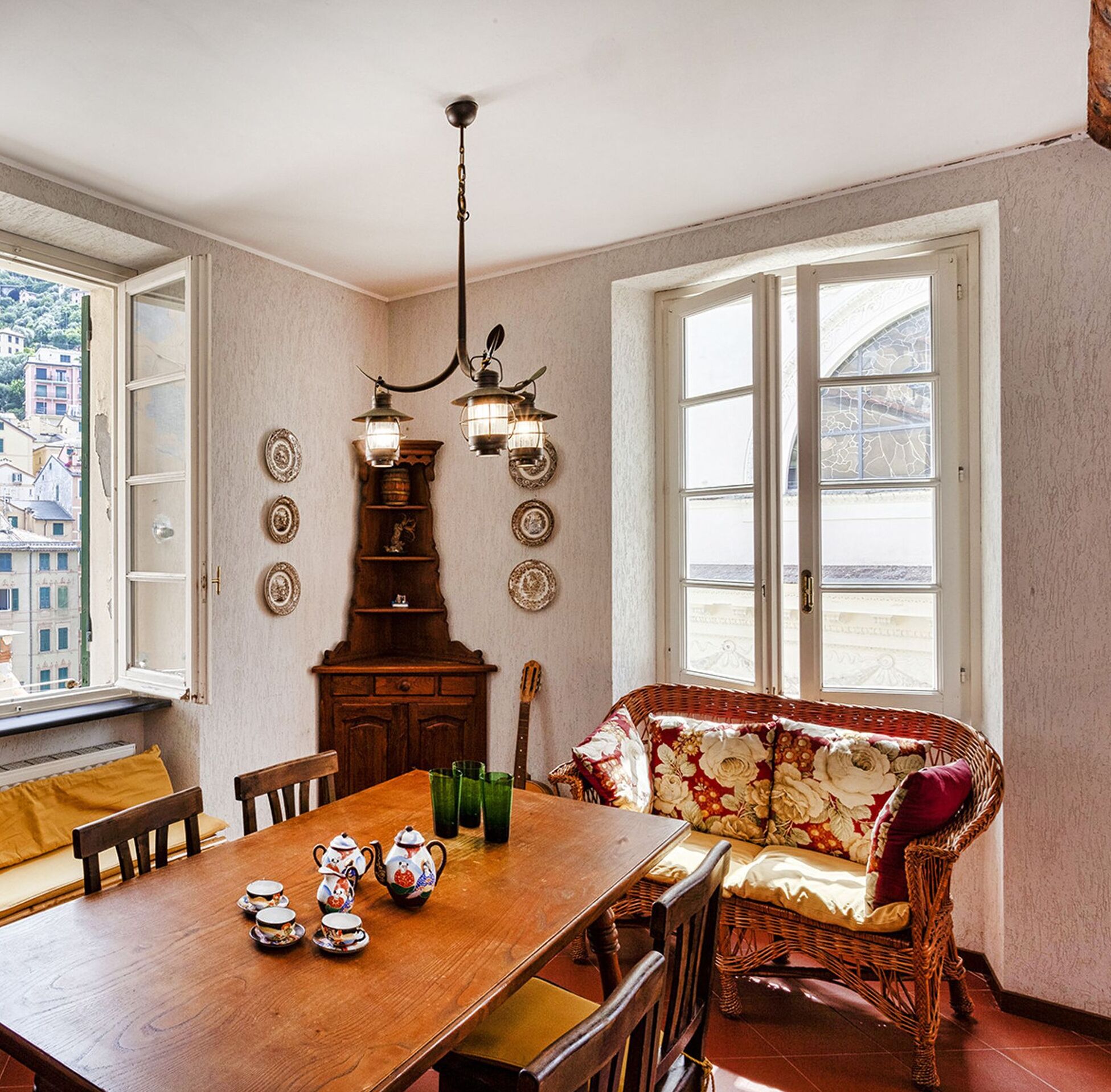 A dining area with a wooden table, chairs, a wicker sofa, and a chandelier.