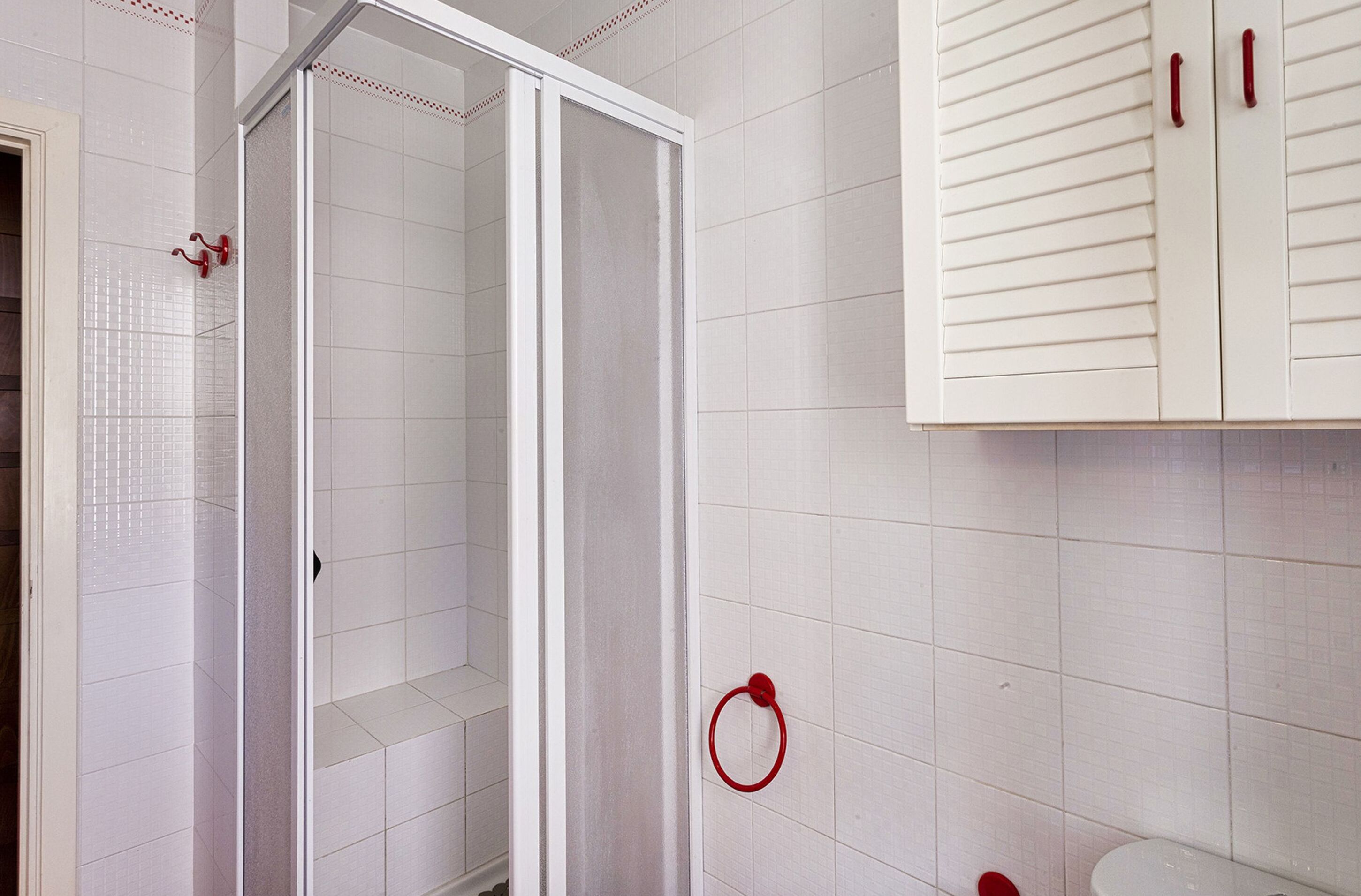Baño con paredes de azulejos blancos, cabina de ducha y retrete.