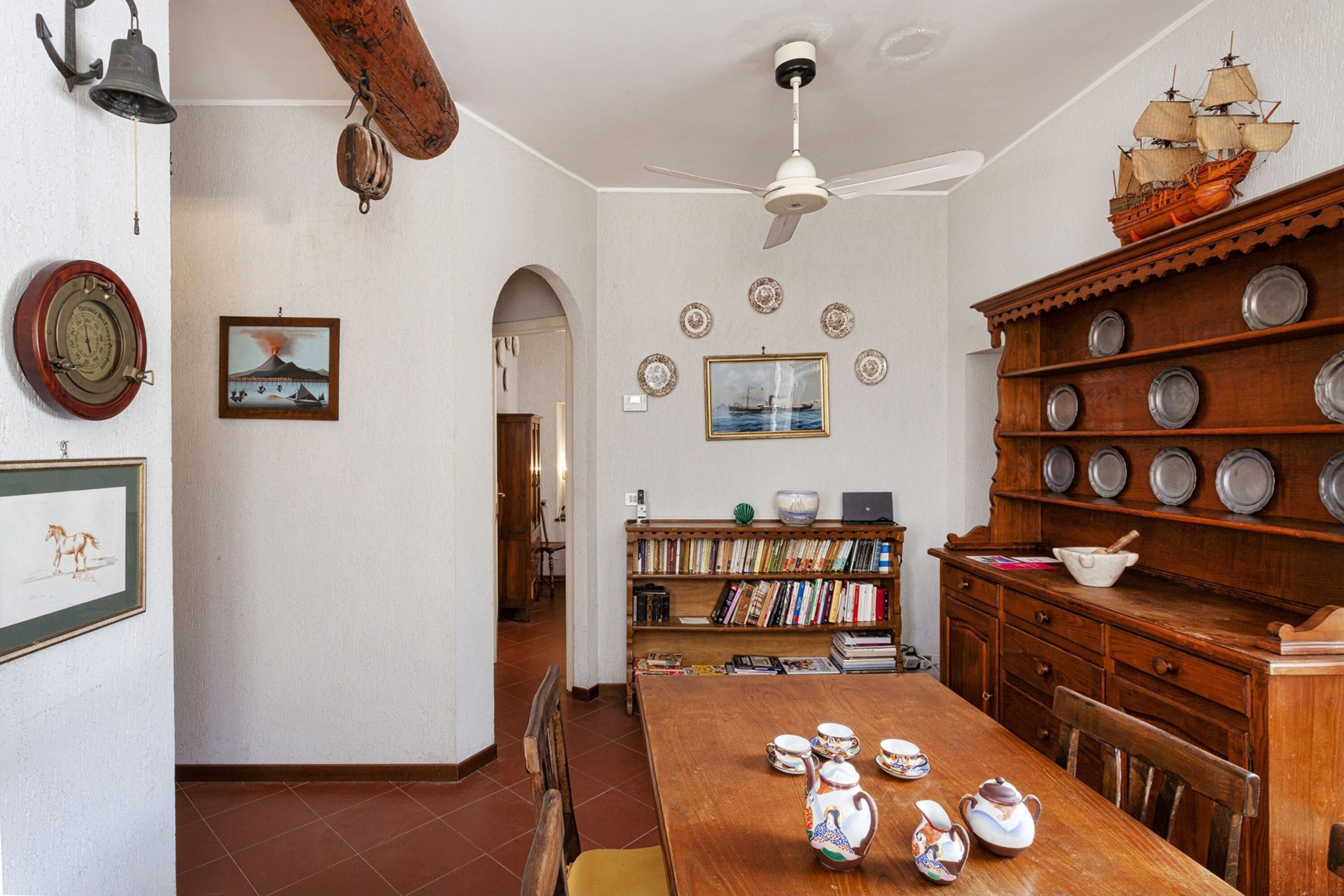 A dining area with a wooden table, chairs, a ceiling fan, and a bookshelf filled with books.