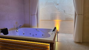 A modern bathroom with a large bathtub, a wooden vanity, and a view of a cityscape through a window. - Baypark Hotel & Spa (Midyat)
