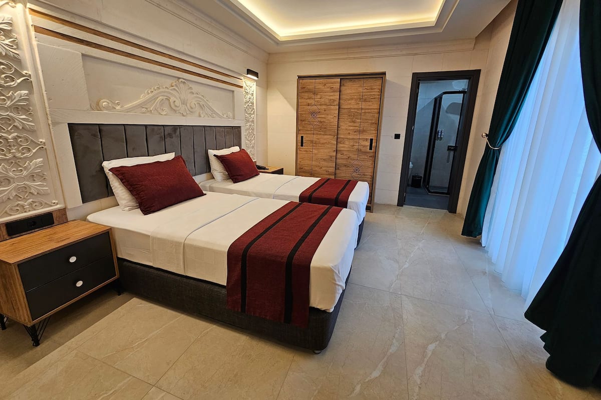 A hotel room with two beds, a wooden wardrobe, a nightstand, and a bathroom door.
