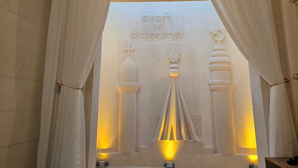 A stone altar with inscriptions and a cross, flanked by curtains and illuminated by wall-mounted lights. - Baypark Hotel & Spa (Midyat)