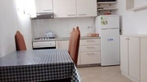 Una cocina pequeña con armarios blancos, estufa, refrigerador y televisor en un estante.