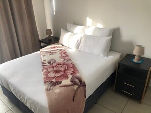 A neatly made bed with white linens, a floral throw blanket, and two bedside lamps on a nightstand. - Exquisite Home In Sandton w/ Pool. Inverter & Gym (Sandton)