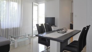 A modern dining area with a glass-top table, black chairs, and a TV on a stand. - Apartments Profaca (Rab)