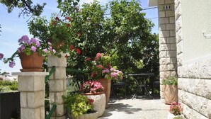 A stone staircase leading to a building entrance, surrounded by potted plants and flowers. - Apartments Profaca (Rab)