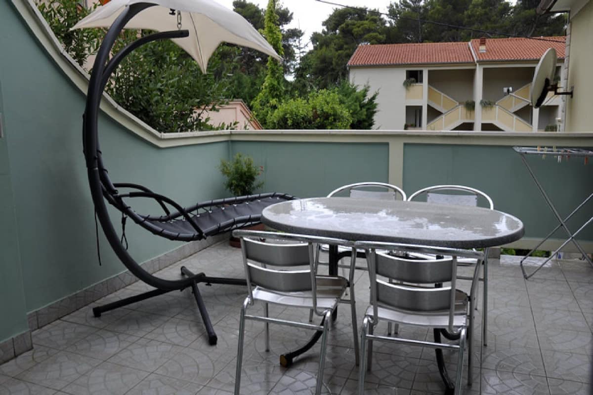 Een terras met een ronde tafel, vier stoelen, een parasol en een schotelantenne.