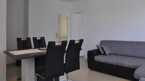 A modern living room with a grey sofa, a dining table with black chairs, and a minimalist design. - Apartments Profaca (Rab)