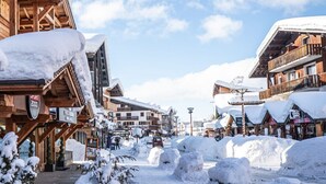 Un pueblo nevado con edificios de madera, cielo despejado y un camino cubierto de nieve.