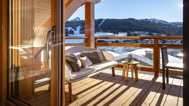 Terraza de madera con sofá y mesa, con vistas a un paisaje montañoso nevado.