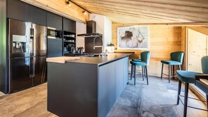 Una cocina moderna con una isla central, muebles de color negro, electrodomésticos de acero inoxidable y techo de madera.