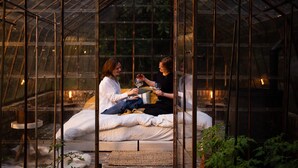 Une serre accueillante et fermée, avec un banc où sont assis deux personnes, chacune tenant un verre de vin.