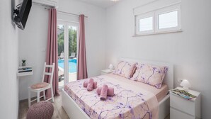 A bedroom with a bed, a desk, a chair, a small round ottoman, a nightstand, and a TV mounted on the wall. - Villa Tomicich (Rasa)