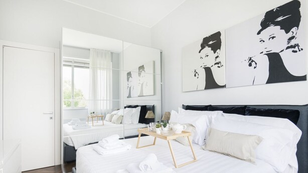 A modern hotel room with a large bed, a bedside table with a lamp, and artwork on the wall. - Easylife - Residential apartment on Navigli area (Milano)