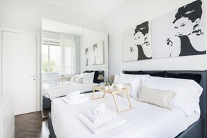 Una habitación de hotel moderna con una cama grande, una mesita de noche con lámpara y una obra de arte en la pared.