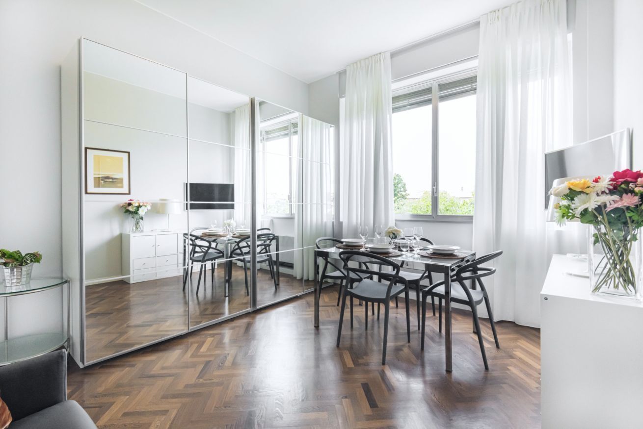 A modern dining room with a large mirror, wooden flooring, and a dining table set for four.