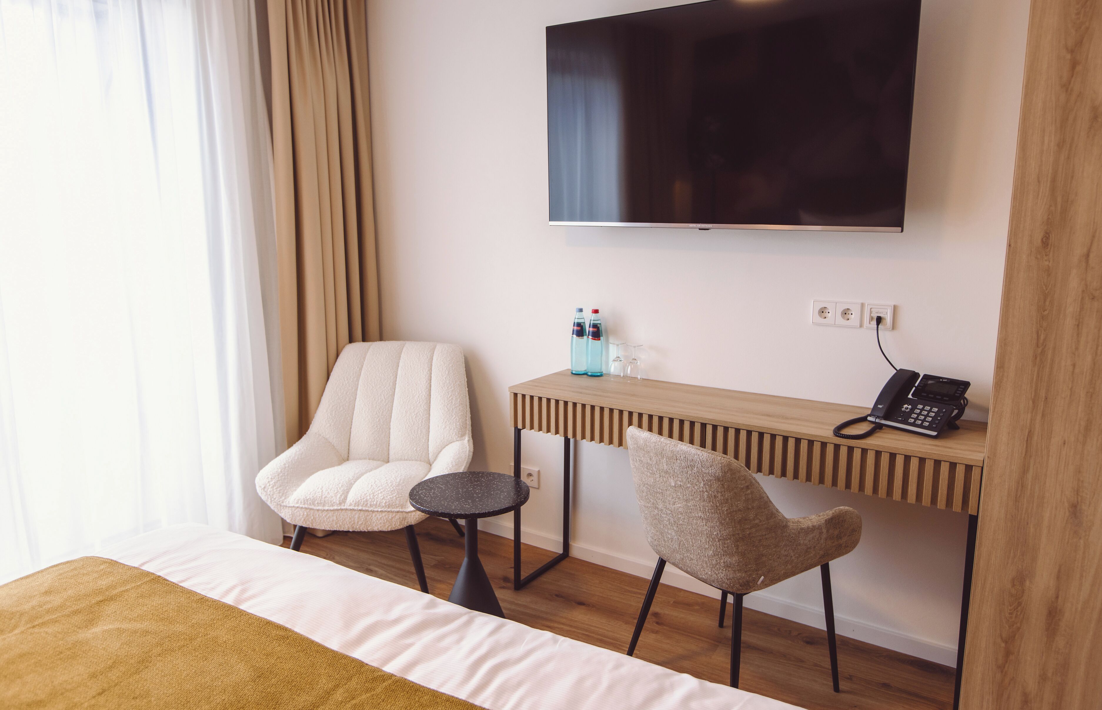 Une chambre d’hôtel comprenant un lit, un téléviseur fixé au mur, un bureau en bois avec un téléphone, deux chaises et une petite table.