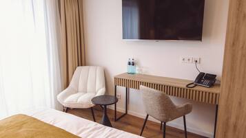 Une chambre d’hôtel comprenant un lit, un téléviseur fixé au mur, un bureau en bois avec un téléphone, deux chaises et une petite table.