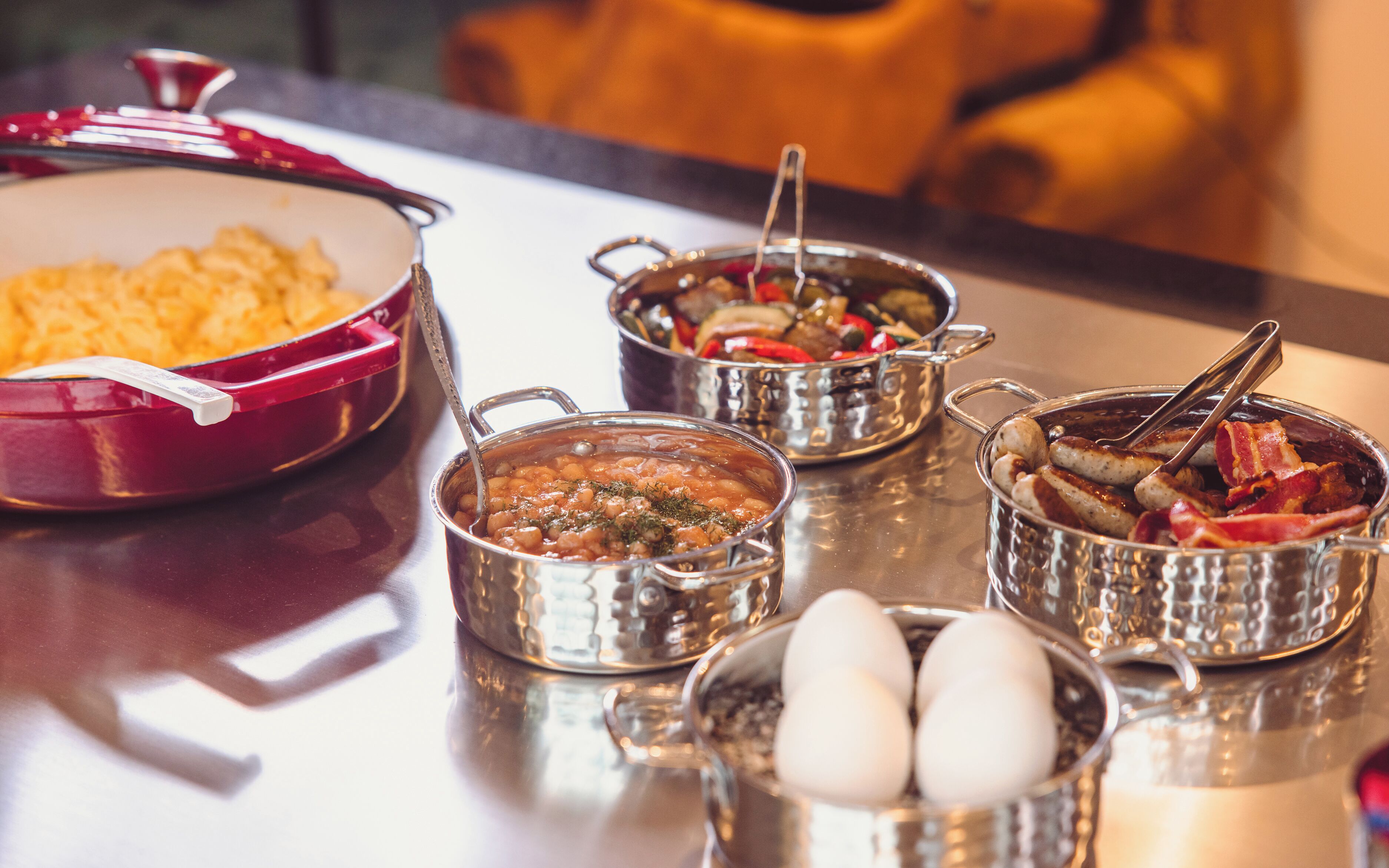 Una mesa con varios platos, incluyendo una olla roja, un tazón de frijoles, un tazón de verduras, un tazón de carne y un tazón de huevos.