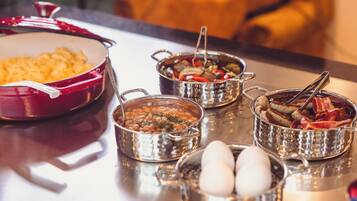 Una mesa con varios platos, incluyendo una olla roja, un tazón de frijoles, un tazón de verduras, un tazón de carne y un tazón de huevos.