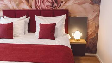 Un lit bien fait, avec une tête de lit rouge et du linge de lit blanc, une lampe de chevet et une fresque florale sur le mur.