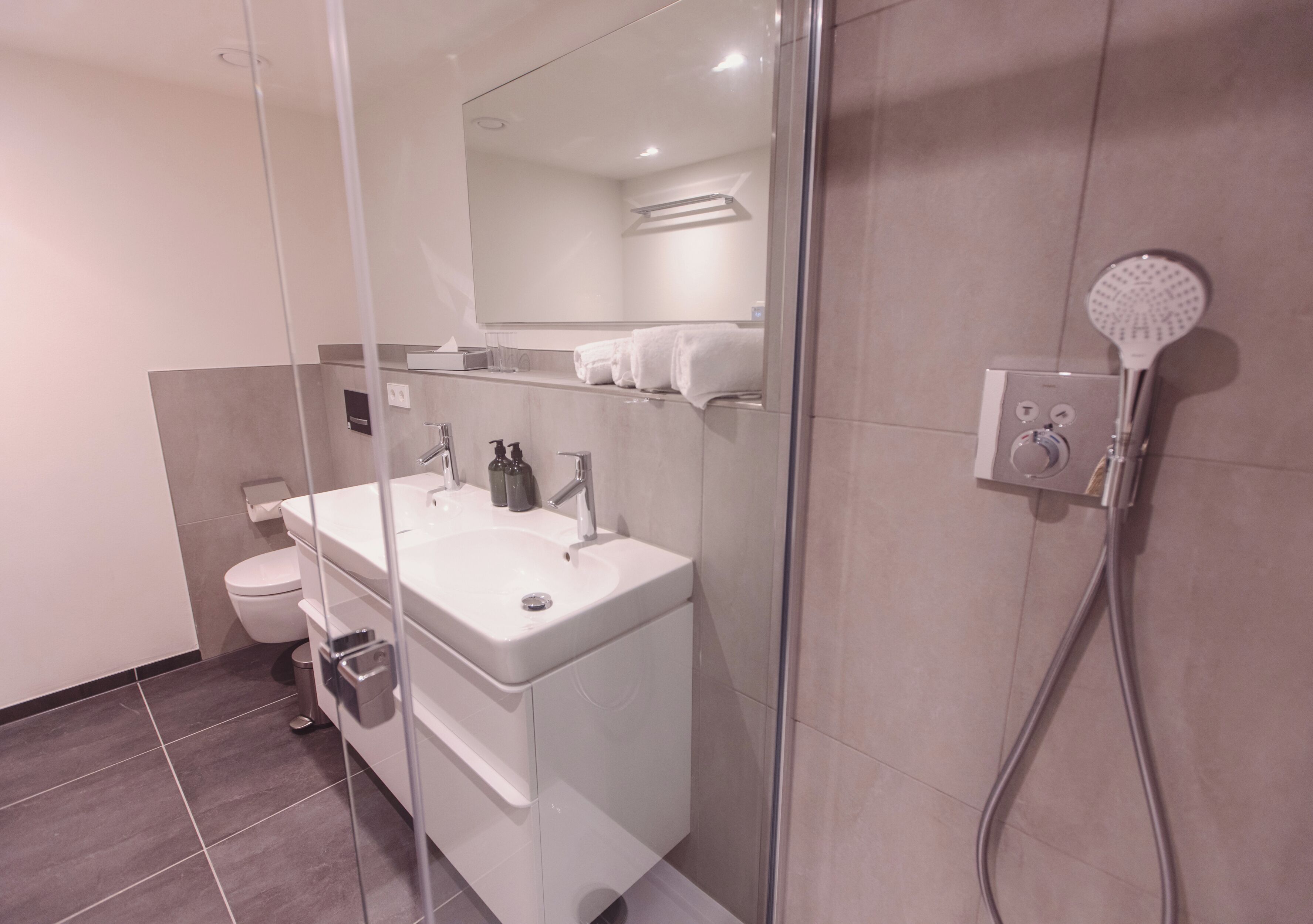 A modern bathroom with a glass shower enclosure, a double sink vanity, and a toilet.